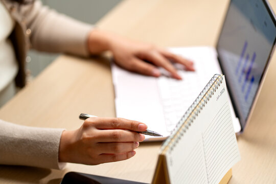 Woman reviewing financial plans with pen in hand beside laptop and June 2025 calendar on wooden desk