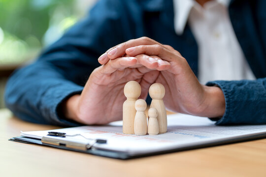 Hands gently cradling wooden family figurines over financial documents on wooden desk