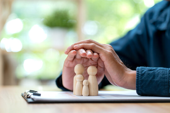 Hands gently cupping wooden family figurines over financial documents on warm wooden desk