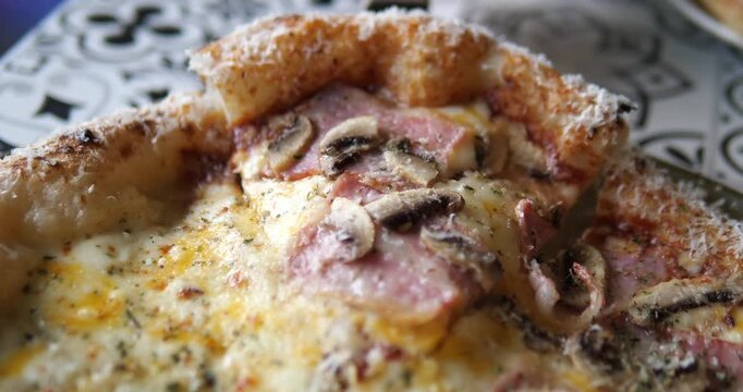 Close up of lifting hot ham and mushroom pizza slice with melted cheese