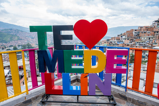 Colorful i love medell&iacute;n sign with heart symbol overlooking comuna 13 favela cityscape in colombia