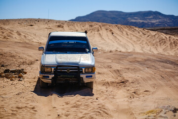 Front view of a white offroad vehicle driving on a sandy desert track under clear sky © Buğra Kaan Ersoy
