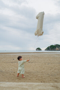 baby boy celebrating first birthday with number 1 balloon on beach.