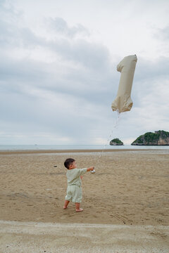 baby boy celebrating first birthday with number 1 balloon on beach.
