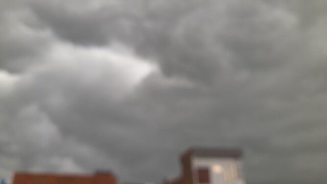Dramatic dark grey storm clouds gather above rooftops, signaling impending heavy rain or severe weather, blurred background