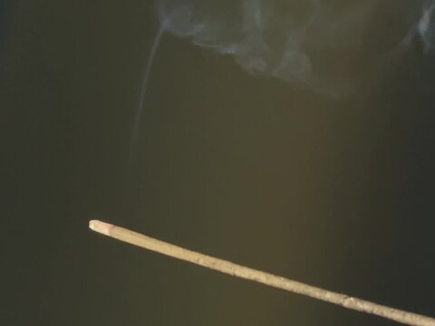 Lit aromatic incense stick releasing pleasantly scented smoke, in a wooden holder. Aromatherapy, meditation, relaxation, spirituality, and yoga concept, with a calming atmosphere.