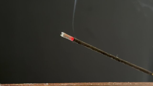 Lit aromatic incense stick releasing pleasantly scented smoke, in a wooden holder. Aromatherapy, meditation, relaxation, spirituality, and yoga concept, with a calming atmosphere.