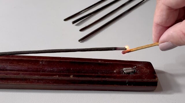 Lit aromatic incense stick releasing pleasantly scented smoke, in a wooden holder. Aromatherapy, meditation, relaxation, spirituality, and yoga concept, with a calming atmosphere.