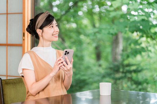 A woman's hands as she operates her smartphone in a cafe overlooking a lush green forest.