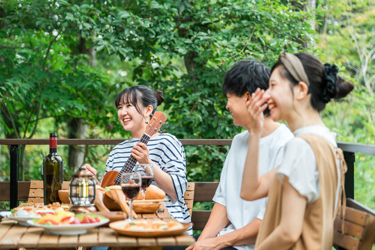 Young Asian men and women, friends, colleagues, and coworkers enjoying a barbecue, home party, and glamping on a wooden deck.