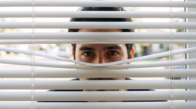 Man peering through white window blinds