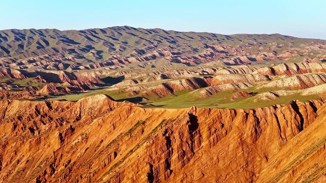 Aerial view of a unique danxia landform showing striated red sandstone mountain ridges under a blue sky along the S101 highway in Xinjiang, China