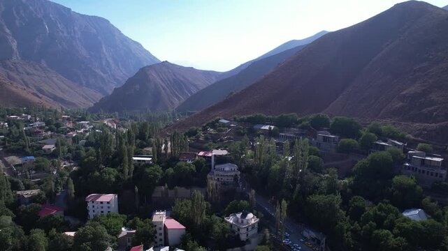 North Road village nestles in trees at the foot of steep mountains, houses scattered through a green highland pocket. Ideal for travel, tourism, and nature stock Iran Alborz mountains.