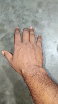 Close-up of a hairy male hand making open and closed hand gestures on a concrete background.