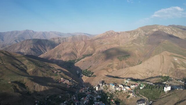 Shem mountain ridges roll under a blue sky, aerial highland folds with a distant settlement tucked in the valley. Ideal for travel, tourism, and nature stock Iran Alborz mountains valleys.