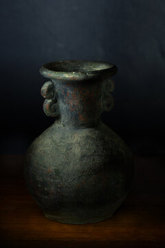 Old pottery vase handcrafted with unique design displayed on wooden surface in dark setting