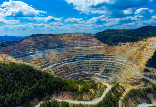 Steep, terraced benches of the Roșia Poieni copper mine, a massive open-pit excavation located in the Apuseni Mountains of Alba County, Romania.