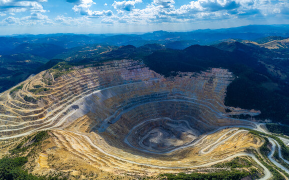 Steep, terraced benches of the Roșia Poieni copper mine, a massive open-pit excavation located in the Apuseni Mountains of Alba County, Romania.