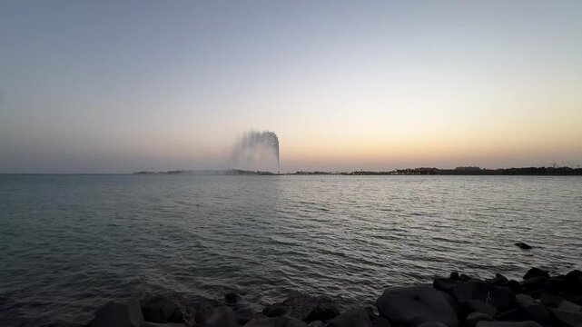 Wide static shot of King Fahd Fountain spraying water high into the sky over the Red Sea in Jeddah at dusk.