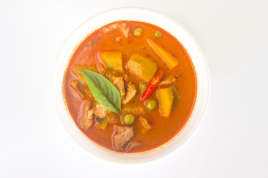 Thai pork and pumpkin curry in white bowl with basil leaf, top view on white background