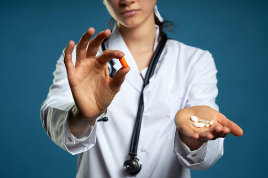 Young female doctor holding a pill, looking at it and giving it as a treatment to the patient