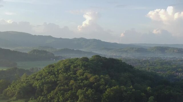 Aerial view of green tropical hills, mist, and village at sunrise. Ideal for travel, nature, and environment concepts