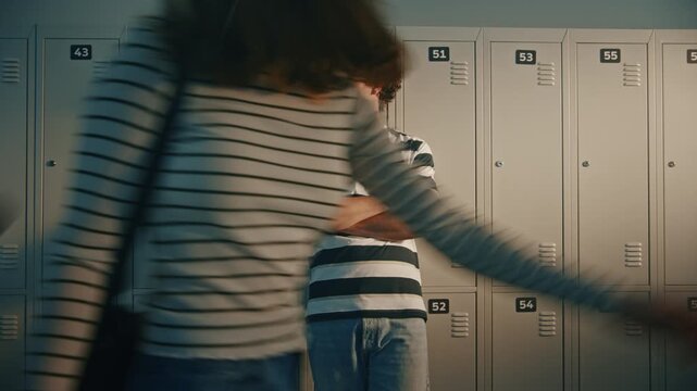 Teenage Boy With Serious Expression Stand Alone Near School Lockers as Other Students Move Through Hallway, Expressing Insecurity, Emotional Distance, Difficult Adolescence. Concept Teenage Lifestyle.