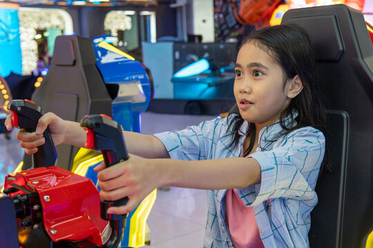 Young Asian girl with a surprised expression playing an arcade simulator game. Family entertainment, recreation concept.