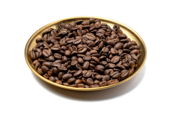 Roasted coffee beans piled on a round gold metal plate isolated on a white background.