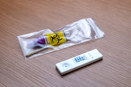 Positive Influenza A rapid antigen test cassette next to a sealed biohazard specimen bag containing a used swab. Home diagnostic testing, seasonal flu infection concept.