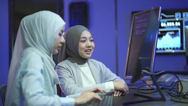 Two Muslim women programmers in hijab collaborating on software code in a modern tech office.