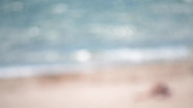 Blurred background. Sea beach sand waves seacoast on sunny summer day. Abstract view of water surface of sea and sandy beach on sunny day with blurry white bokeh spots from sun glare on surface of sea