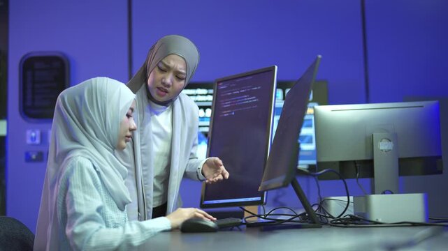 Two Muslim female developers in hijabs looking stressed and confused while troubleshooting code on multiple computer screens