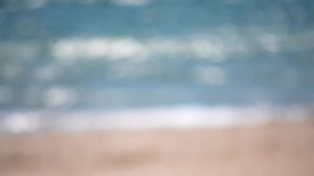 Sea sand beach. Sea waves seacoast on sunny summer day. Abstract view of water surface of sea and sandy beach on sunny day with blurry white bokeh from sun glare on surface of sea. Blurred background