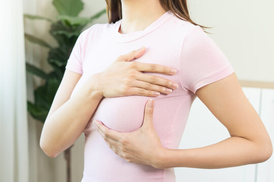 Health care breast cancer checking concept. Asian young woman, girl doing self check of breast cancer on pink t-shirt in room at home on white wall. How do I check breast cancer prevention awareness.