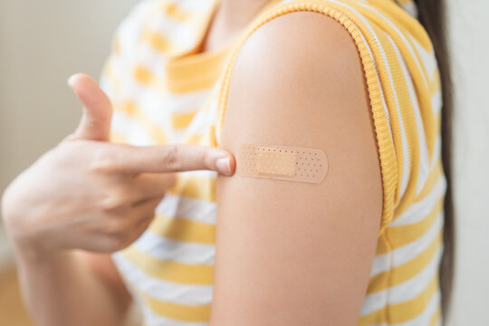 Close up of a young woman pointing at an adhesive bandage on her arm after receiving a vaccine injection, representing healthcare, virus immunity protection, and prevention.