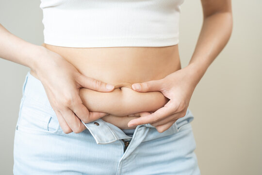 Weight gain, overweight, high cholesterol and pressure, woman hand pinching excess fat big belly with finger and wear tight trousers, show fat around abdomen body, getting loss, isolated on background