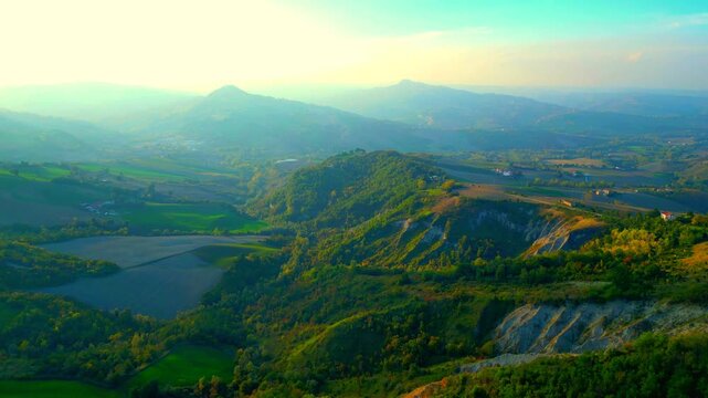 Refreshing aerial push-in truck right pan left shot near Santa Vittoria in Matenano, mystical sunlight imbuing the horizon with a hazy, mysterious quality, spiritual views of Sibillini Mountains peaks