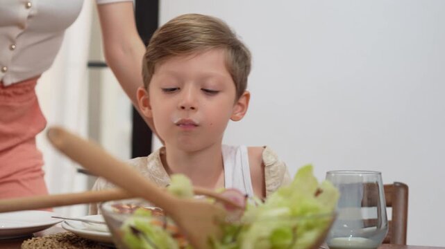 Happy child having lunch with pizza and milk indoors, cute little boy eating pizza and drinking milk at dining table, little boy eating slice of pizza and drinking from glass at home