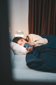 Asian woman sleep on bed at night in bedroom using smartphone social media addiction, dating online with digital communication