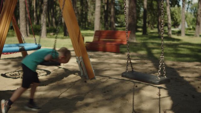 Young boy riding a chain swing at an outdoor park playground. Child learning to swing at a park on a warm sunny day. Outdoor activities for kids. Active child playing at a playground in a park.