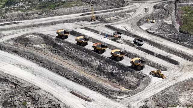 An aerial view of rigid dump trucks and excavators parked in a row at a coal mine