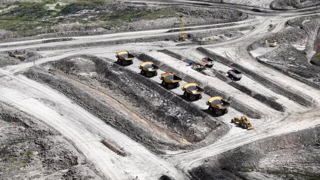 An aerial view of rigid dump trucks and excavators parked in a row at a coal mine
