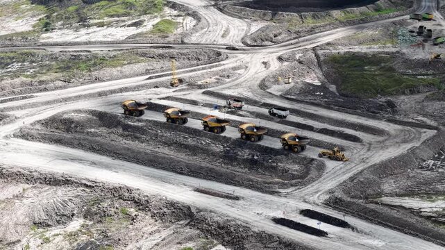 An aerial view of rigid dump trucks and excavators parked in a row at a coal mine