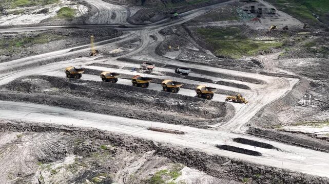 An aerial view of rigid dump trucks and excavators parked in a row at a coal mine