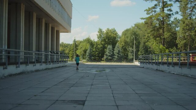 Active child chasing birds on a massive terrace outside a large public building. Wide shot of a young boy running across a plaza and scaring of pigeons. Kid running around a park.