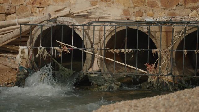 Industrial wastewater or chemical discharge flowing into the sea through a clogged, rusty metal drainage grate, Environmental pollution and industrial waste concept.