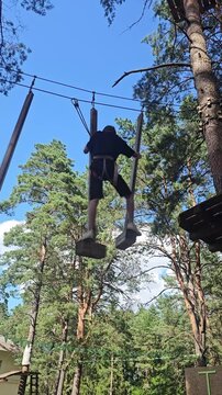 Person swings on a rope in a forest during a sunny day while wearing safety gear