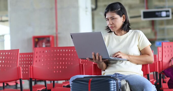 Young woman working on a laptop with luggage at Train station, Bus station, Airport waiting area, remote work, digital nomad lifestyle, business travel, productivity, and modern travel