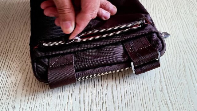 Opening zipper on dark brown leather satchel indoors, showing accessory detail, compartments, texture, and everyday use for fashion, travel, storage, and personal organization